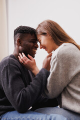 Smiling diverse couple in casual clothes and jeans hugging at home 