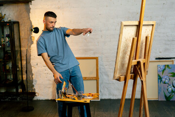 Obraz premium in an art workshop an artist in a blue T-shirt measures with brush on canvas and thinks