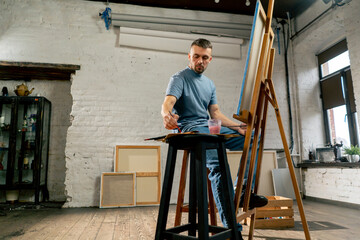 general shot young artist in a blue t-shirt in an art studio working on painting while sitting