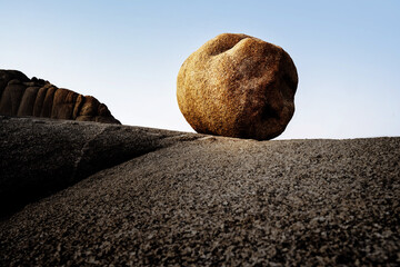 An almost round ball of rock lies illuminated by the golden sun on a plateau against a blue sky.