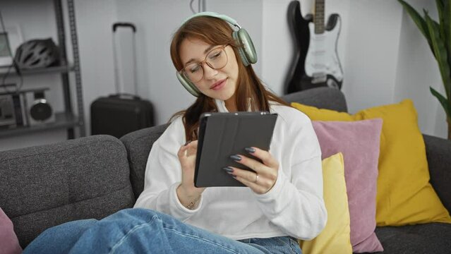 Young woman wearing headphones enjoys tablet in cozy living room
