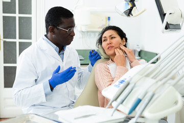 Asian woman complaining about toothache to african-american man dentist during consulatation in...