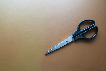 close up of a pair of closed scissors on a brown leather background 