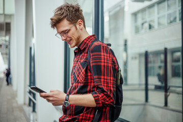 A young traveler leaning at metro station and smiling at phone.