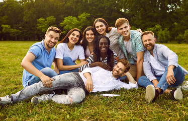 Fototapeta premium Portrait of a group of happy people friends sitting in the summer park hugging and smiling. Young students looking cheerful at camera outdoors. Friendship and togetherness concept. Banner.