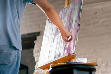 low shot in an art workshop an artist in a blue T-shirt draws on a canvas with palette knife
