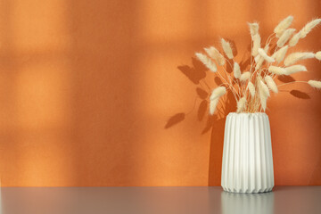 Vase with dry flowers against orange background with shadow pattern