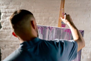close up in an art workshop an artist in a blue T-shirt creates pink smudges with brush on canvas