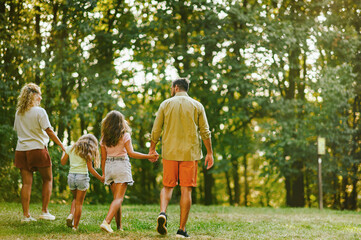 Rear view of a happy family holding hands and taking a walk in nature.