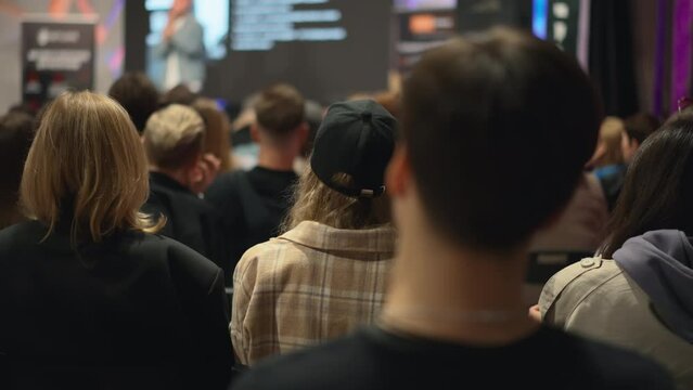 Panning audience of people at seminar in conference room. Young adults men and women sit in loft-style venue, embodying vibrant startup ecosystem and entrepreneurial spirit