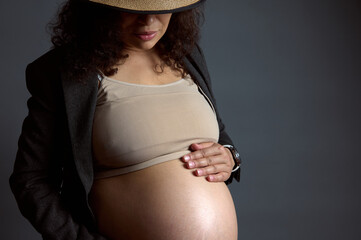 Close-up portrait of young beautiful pregnant woman gently caressing her belly, enjoying her happy...