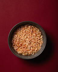 Bowl of noodles in dark ceramic bowl on dark red background