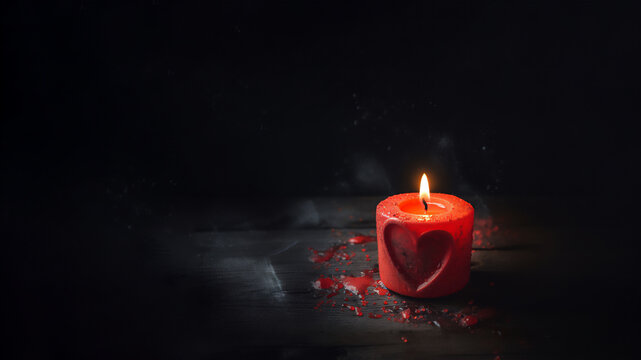 A red candle with a heart image burns on a dark background. Copy space. High quality photo