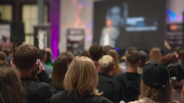 Entrepreneurs gather, attentively listening to success stories at a youth-led business workshop. Millennial crowd focuses on speaker at an entrepreneurship conference, fostering startup innovation.
