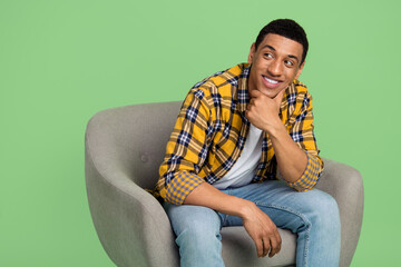 Photo of minded creative person sit comfy chair arm touch chin look empty space isolated on green...