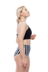 A young girl in a sports swimsuit. A cute blonde girl in a black top and striped panties stands and looks up. Activity, health and positivity. Isolated on a white background. Side view. Vertical.