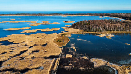 Wooden Bords Trail Through the Kaniera Lake Reeds Aerial Spring Shot Lapmezciems, Latvia. Frozen Lake and Baltic Sea in the Background. Early Spring in Latvia, Kemeri National Park. Slow Motion Shot