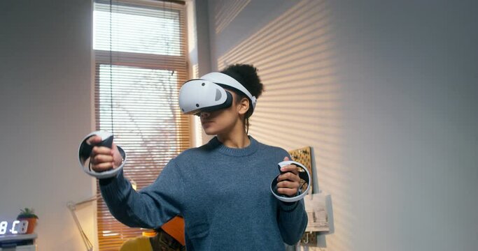 A young woman in a virtual reality headset uses a joystick while standing in the office