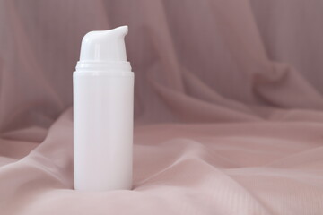 white cream bottle on wavy monochrome surface of soft fabric.