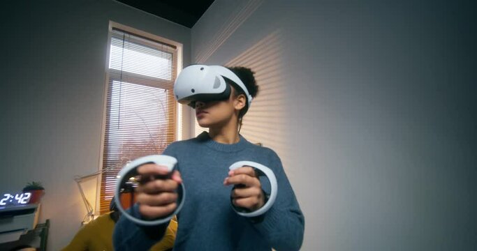 A young woman in a virtual reality headset uses a joystick while standing in the office