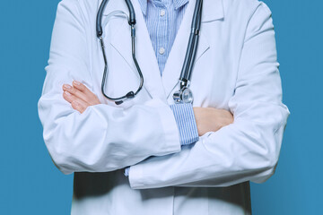 Close-up of crossed arms of female doctor in white lab coat on blue background