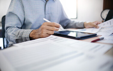 Businessman in office using tablet with documents and chart for analyzing data of investment to make investment plan for a future, financial investment concept.