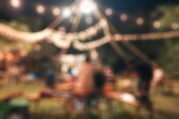 Blurred scene of group of friends with BBQ picnic party and illuminated campfire in backyard