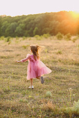 Fototapeta na wymiar Rear view of pretty little girl in tulle pink dresse running on nature at summer sunset. Love. Happy childhood concept