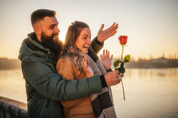 Happy man giving red rose to his woman while they enjoy spending time together on a sunset.	