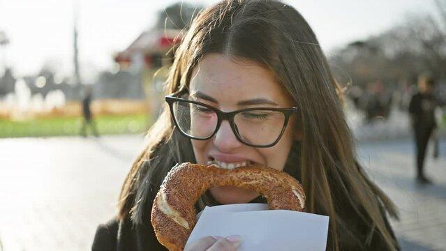 Young woman enjoys a simit on istanbul street, embodying travel, cuisine, and turkish culture in a vibrant urban european setting.