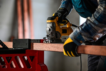 worker in overalls and wearing yellow gloves sawing wood with a reciprocating electric wood saw -...