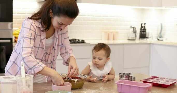 mom and little baby daughter is preparing dough for muffins with berries. mom kiss her daughter