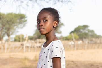 african girl with a proud expression , in the village, standing in front of the kraal with small...