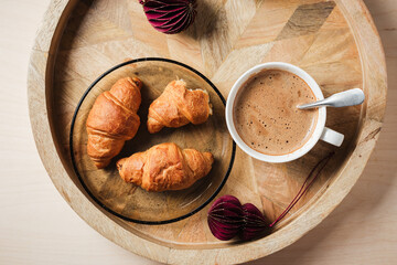 Cup of coffee, chocolate croissants on a wooden tray.