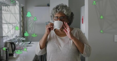Animation of network of connections with icons over senior african american woman drinking coffee - Powered by Adobe