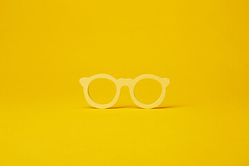 Yellow wooden eyewear frame isolated on the bright solid fond plain yellow background, ilustration optics concept
