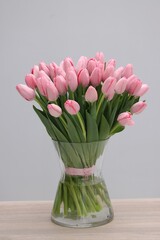 Bouquet of beautiful pink tulips in vase on wooden table against grey background