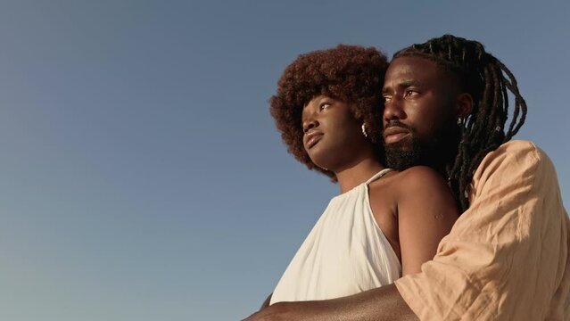 Romantic African couple embracing lovingly outdoors with a clear blue sky in background, showcasing both fashion and affection.