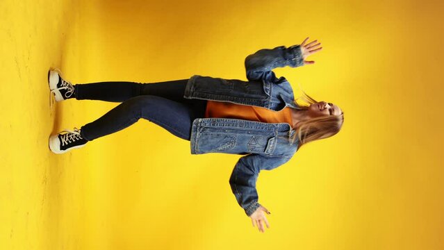 Cheerful young woman with red hair and freckles dressed retro style outfit dancing against yellow studio background. Concept of human emotions, self-expression, hobby, relax. Vertical orientation Ad
