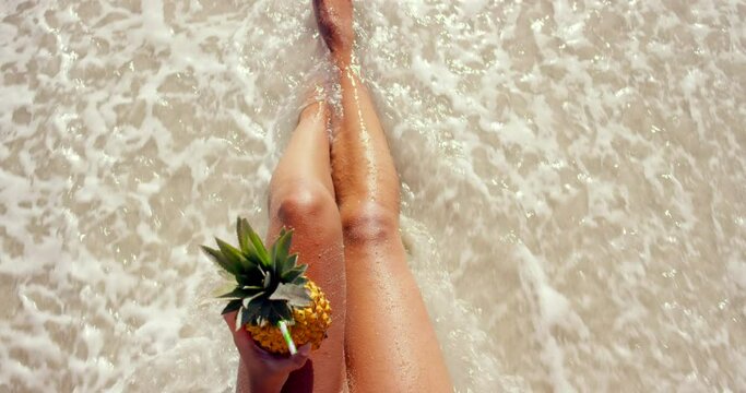 Legs, water and fruit at beach on vacation, peaceful and zen at tropical destination or holiday. Above, pineapple cocktail and calming waves by paradise, nature and person feet for travel in mockup