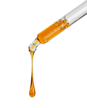 Stretched drop of a yellow oily liquid dripping from a pipette close up isolated on a white background