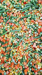 Frozen vegetables in a store, close-up. A mixture of vegetables is sold in the refrigerator in the supermarket. A mixture of peas, corn, green beans, peppers and carrots. View from above. Background