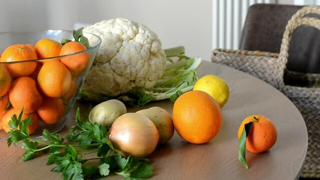 The table is full of Vegetables and Fruits. A female person in a blue sweater approaches the table, takes several citrus fruits: Lemons, Oranges, Tangerines. Scene with hands close up. Organic Food.