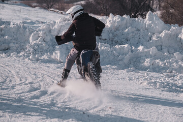Motorcycle racer on motorcycle riding snowy turn. The enduro bike riding on a rural snowy road. 