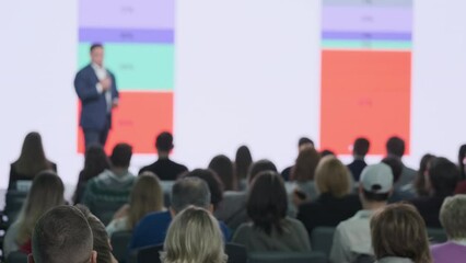 Back view real time of people sitting in hall and listening to influencer presenting startup strategy and showing statistics on big screen during seminar