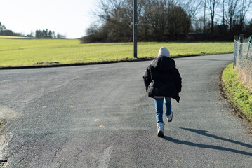 Little girl running on a country road in spring, back view.