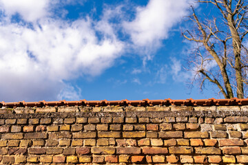 old brick wall with red roof tiles and a view of a blue sky