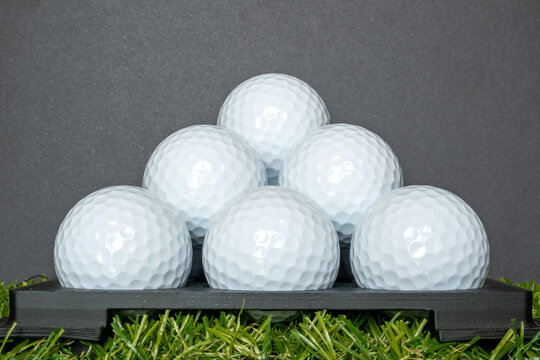 Close-up image of some plain white golf unbranded golf balls stacked up upon each other in front of a black background.