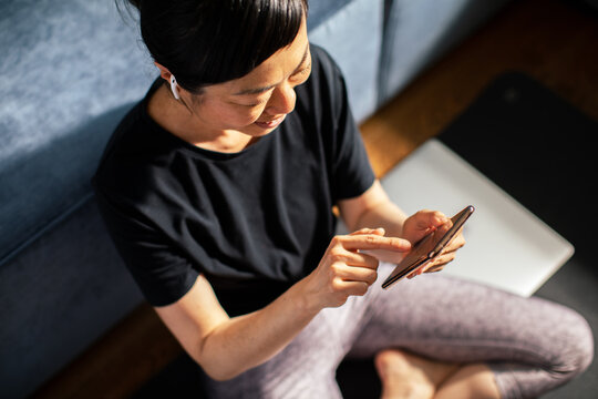 Smiling woman using smartphone on yoga mat at home