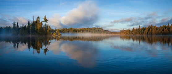 Panorama of blue lake in northern Minnesota with an island and pines on a foggy September morning